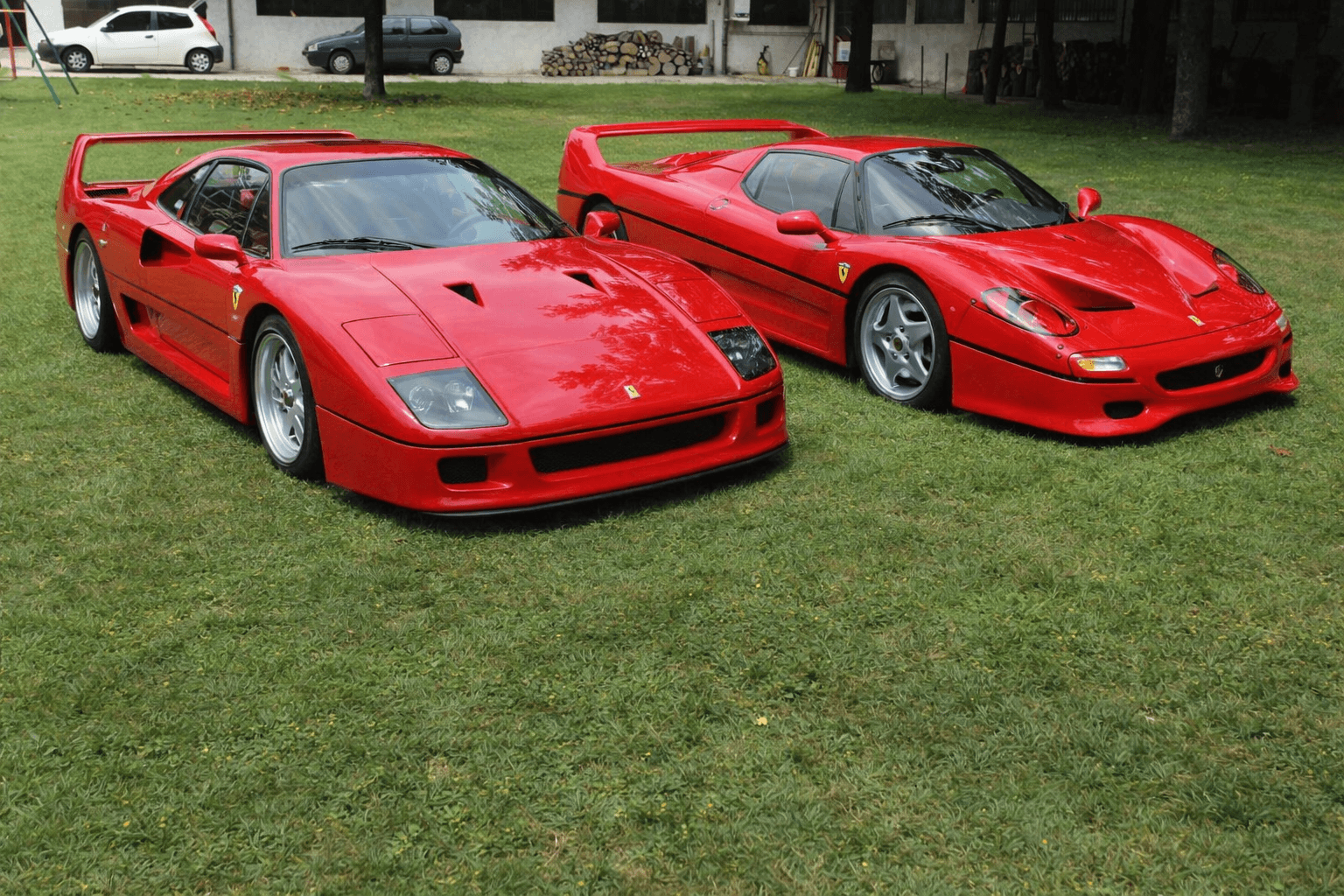 Two red Ferrari supercars, an F40 and an F50, parked on a green lawn.