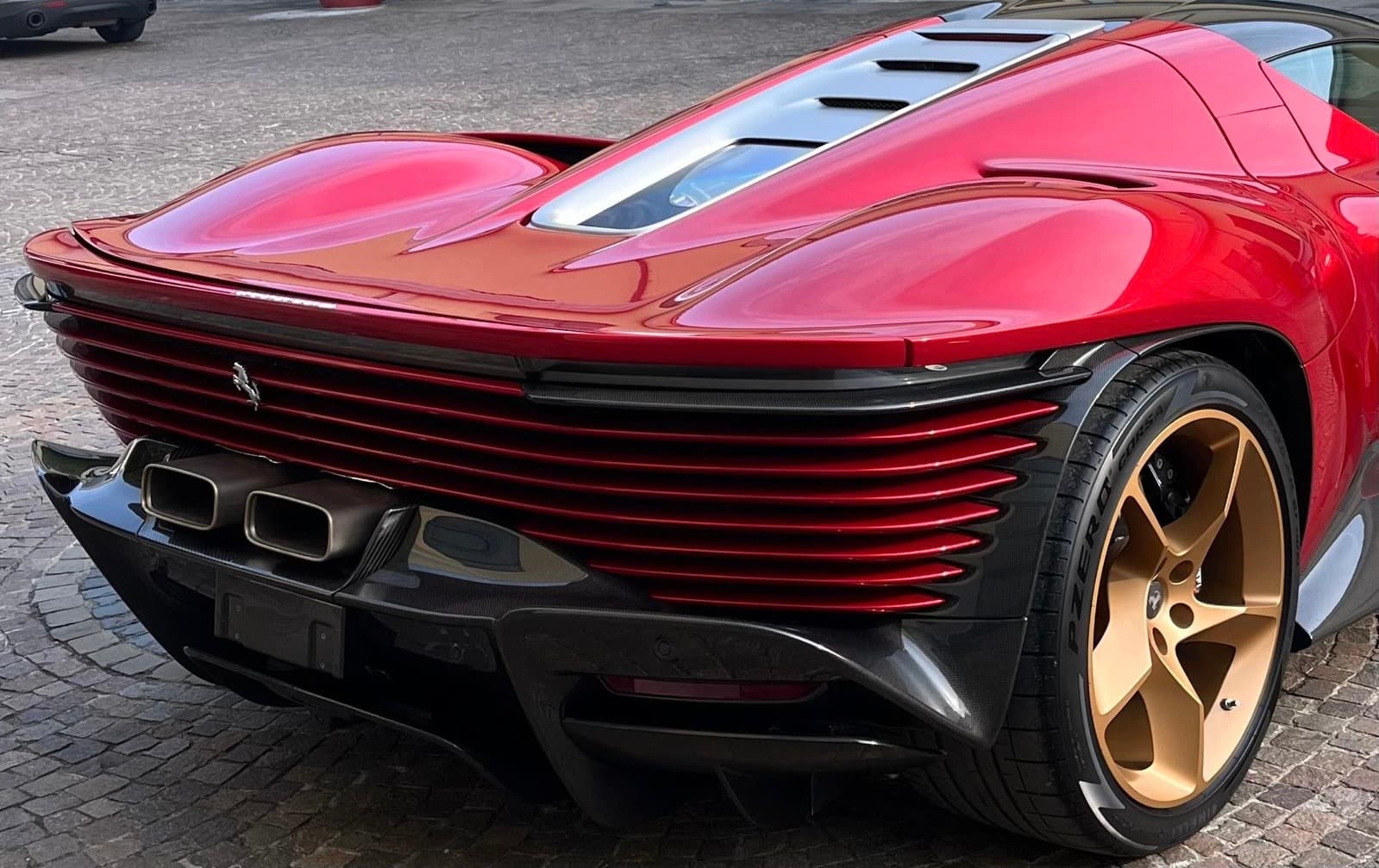 Rear of a red Ferrari Daytona SP3 featuring horizontal slats, central exhaust, and gold wheels.