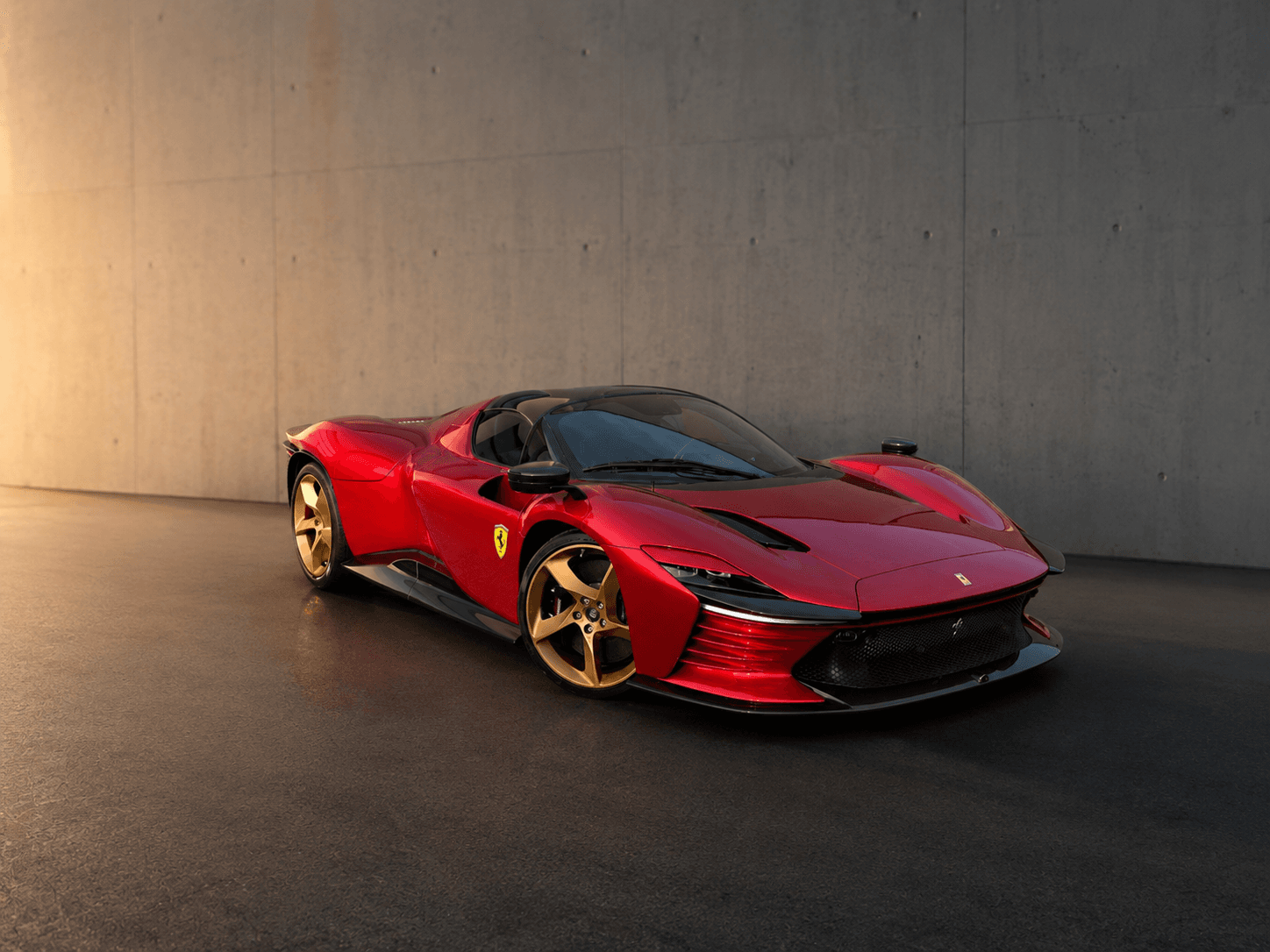 Sleek red Ferrari Daytona SP3 with gold wheels parked in front of a concrete wall.
