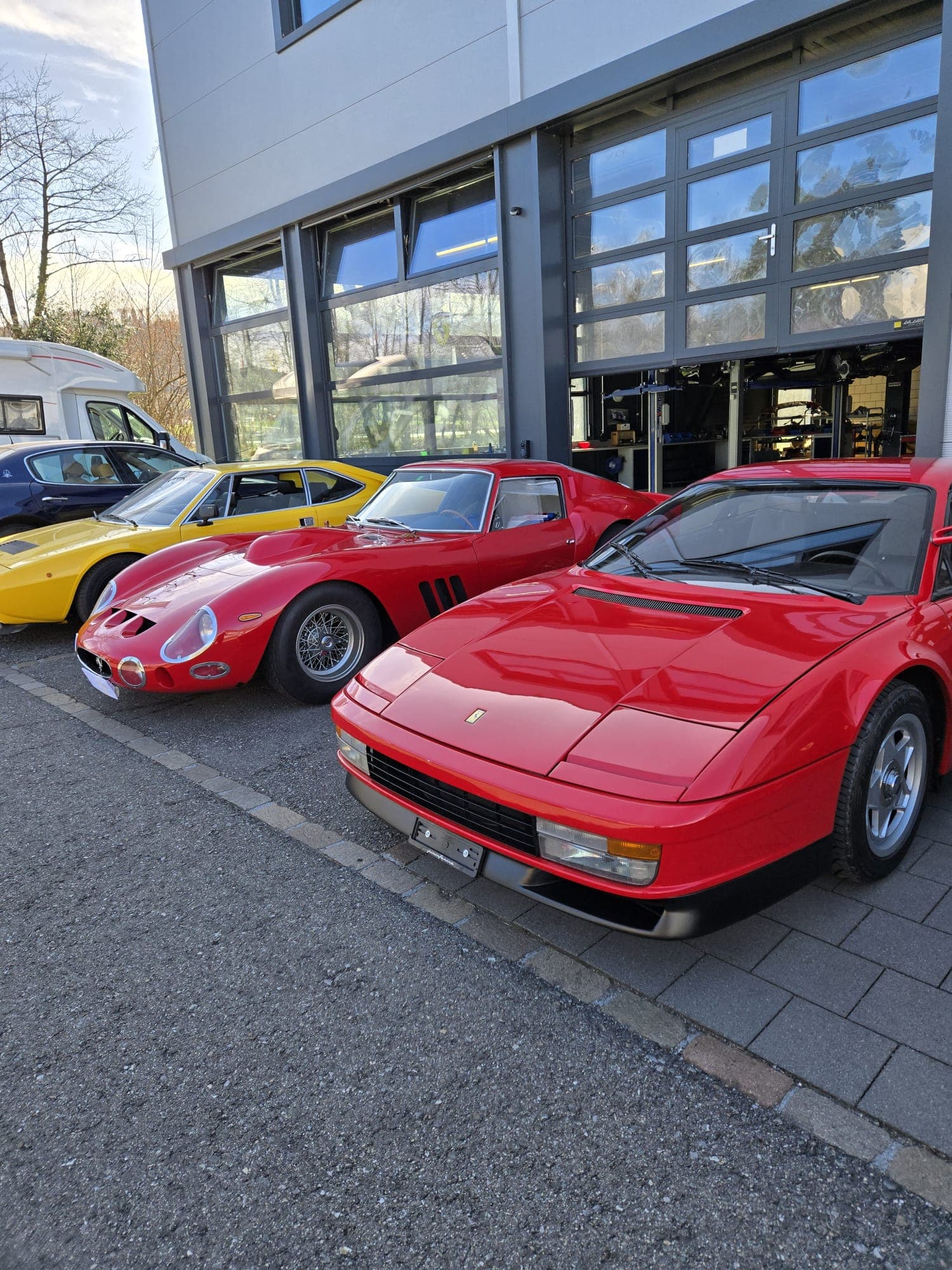 Classic red and yellow Ferrari sports cars parked in a row outside a modern garage.