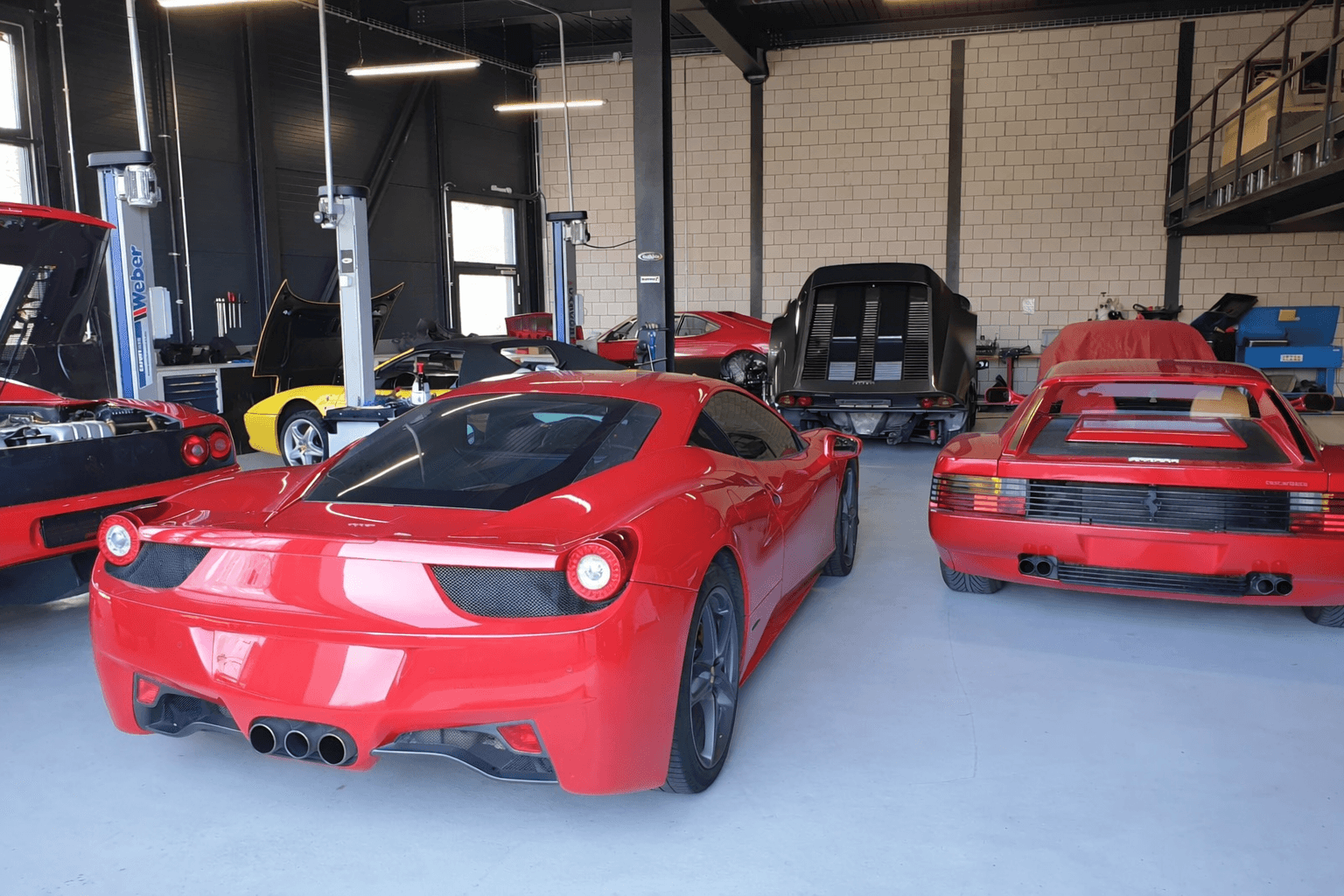 Several red and yellow Ferraris parked inside a professional automotive repair workshop with car lifts.