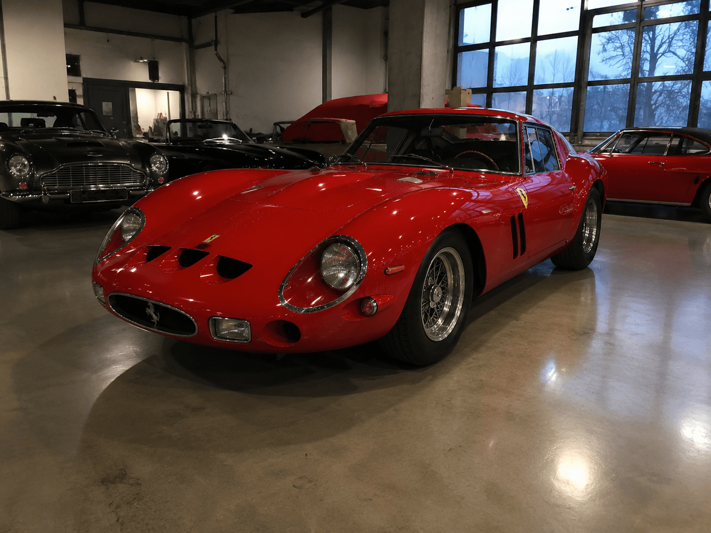 Red vintage Ferrari 250 GTO sports car parked in a garage with other classic cars.