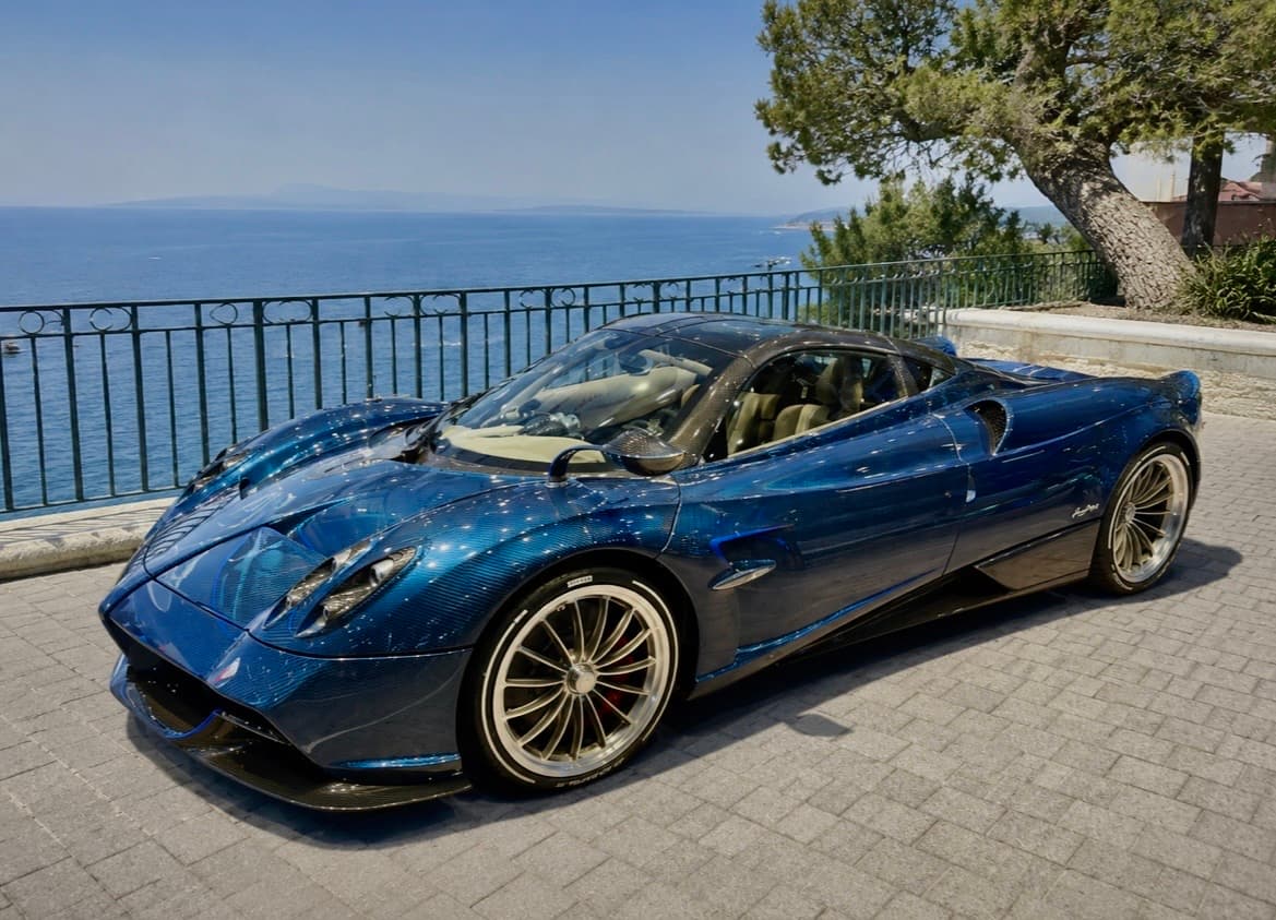 Blue carbon fiber Pagani Huayra parked on a stone terrace overlooking the blue ocean.