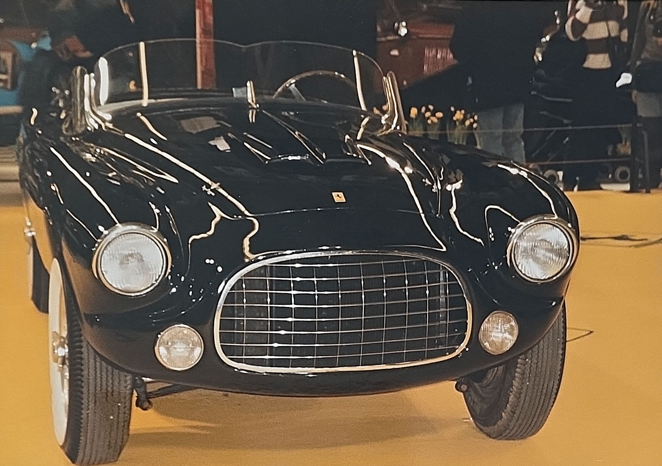 Glossy black vintage Ferrari convertible with a chrome grille and round headlights on display.