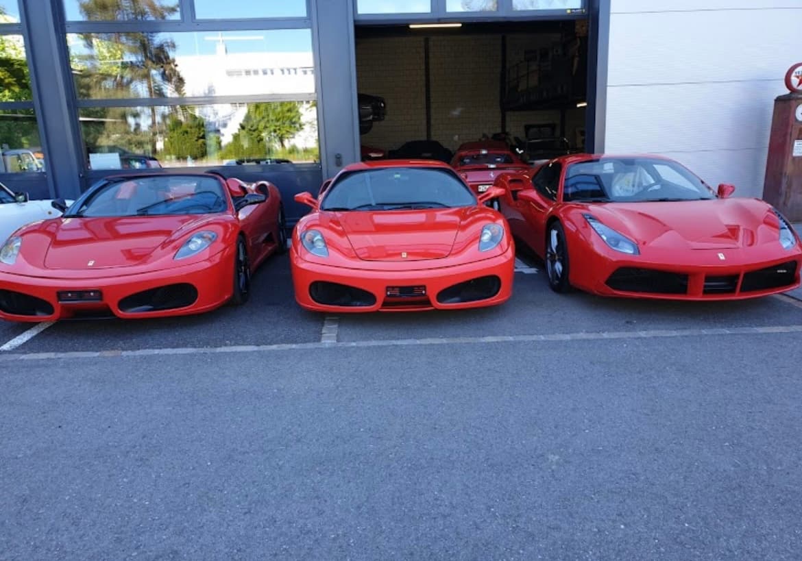 Three red Ferrari sports cars parked in a row outside a modern glass garage.