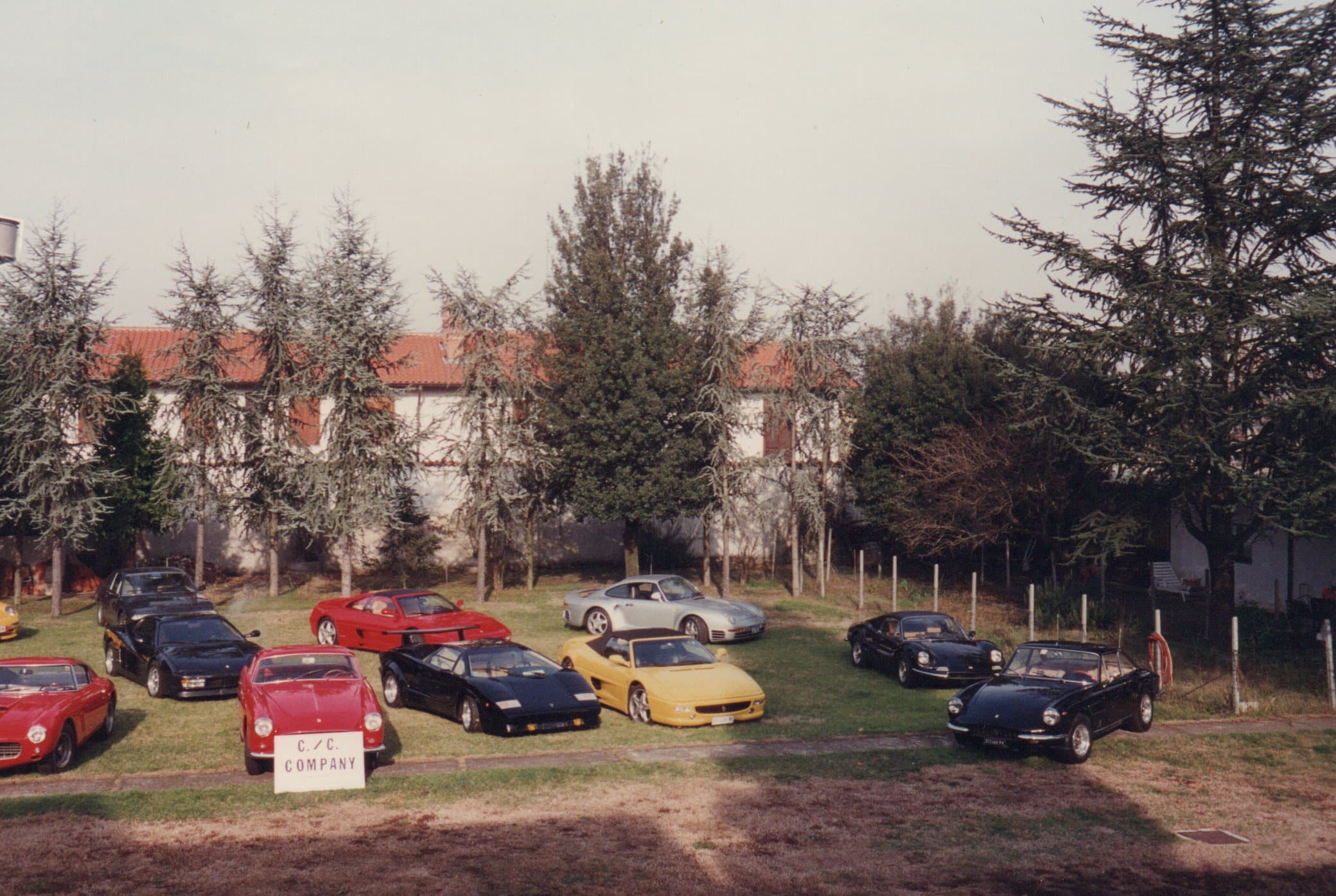 Classic luxury sports cars including Ferraris and a Lamborghini parked on a lawn near trees.