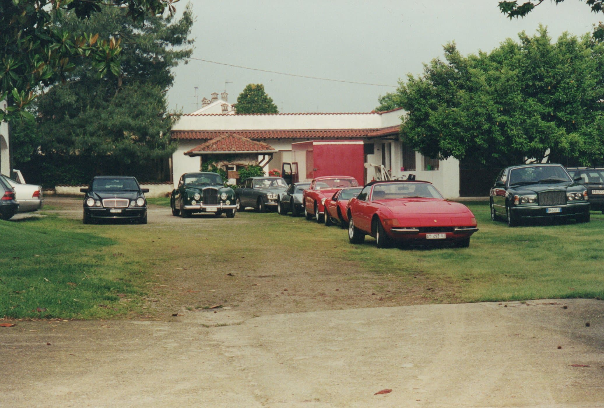 A lineup of classic luxury cars, including a red Ferrari, parked on a grassy estate.