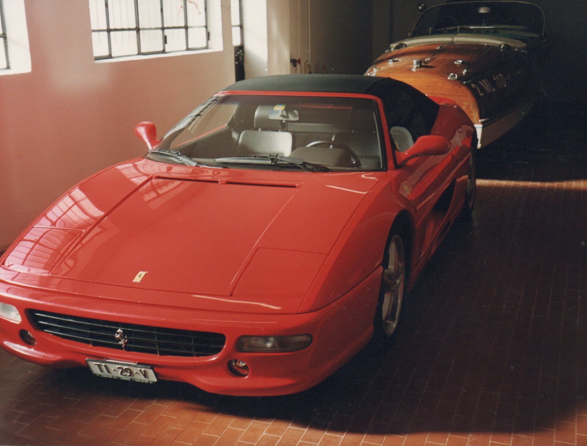 Red Ferrari F355 Spider sports car parked in a garage with a wooden speedboat.
