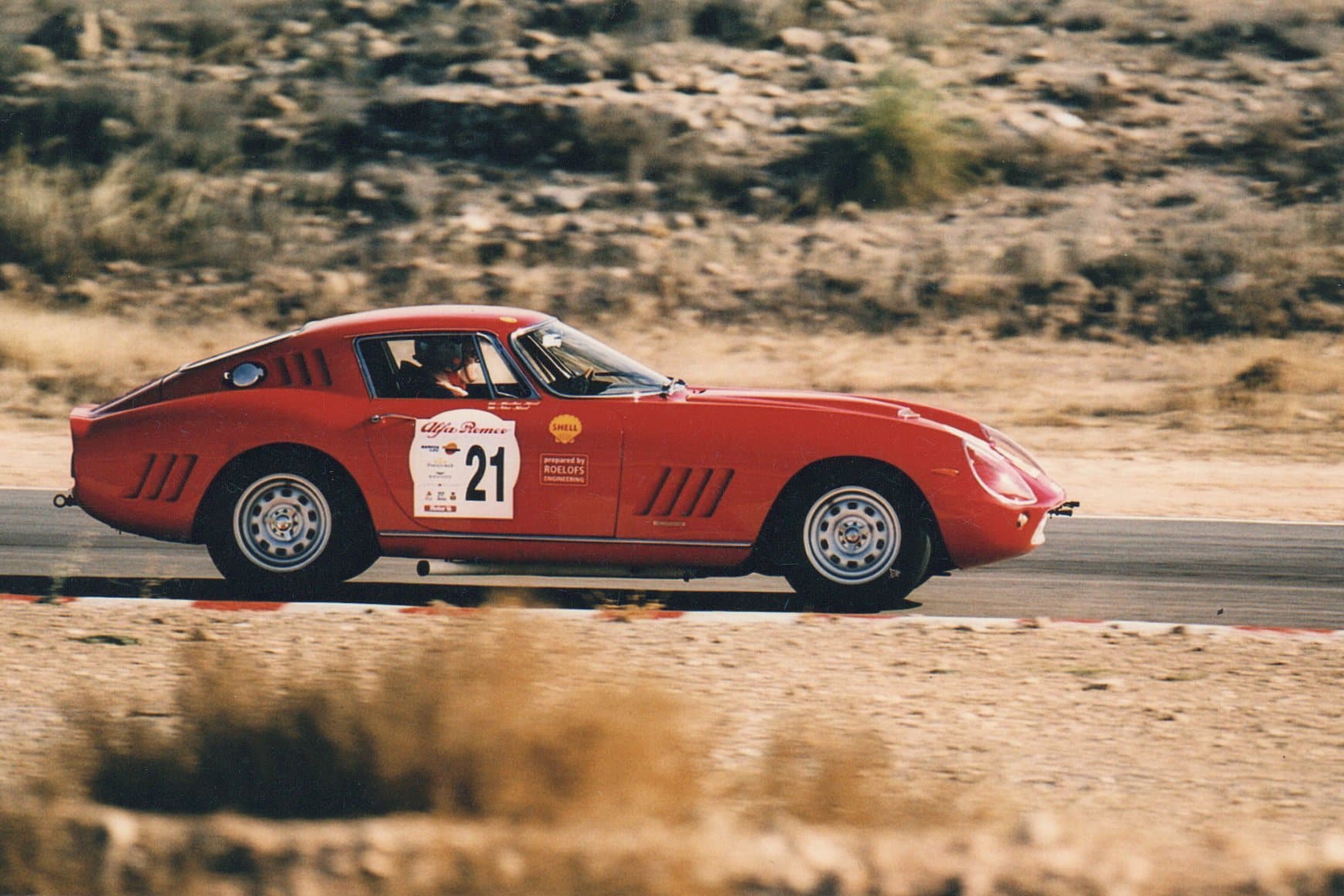 Vintage red Alfa Romeo race car number 21 speeding on a sunny desert racetrack.