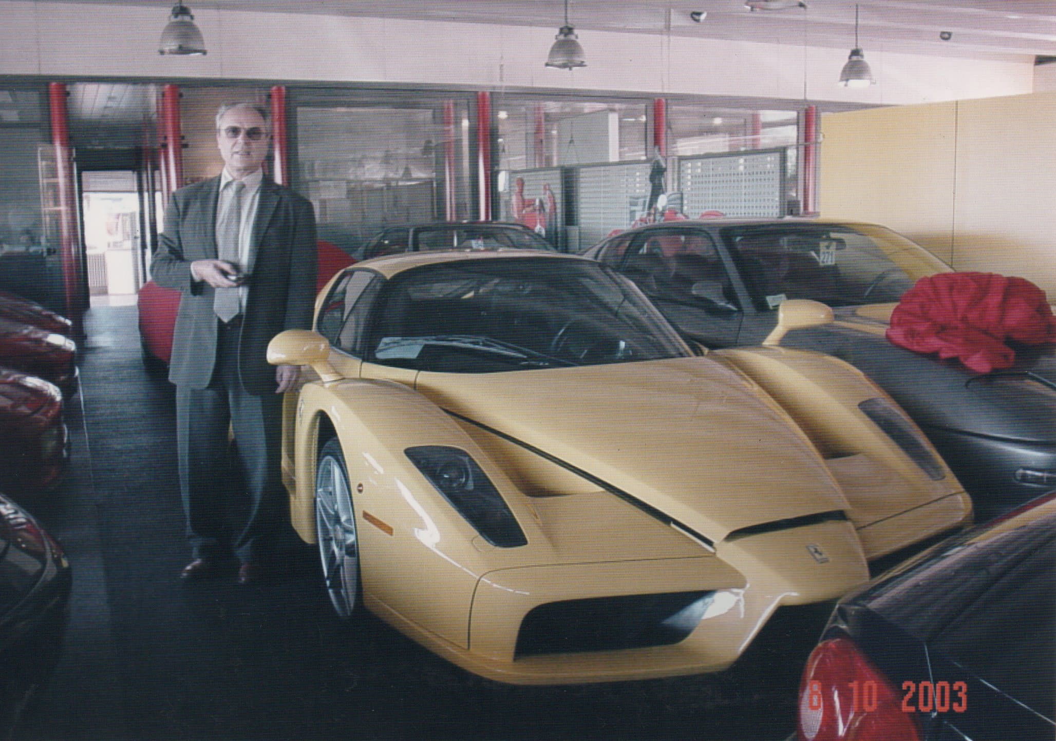 Man in a suit standing next to a yellow Ferrari Enzo in a car showroom.